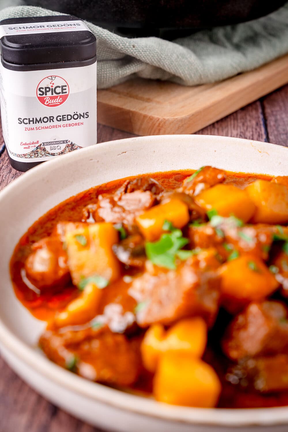 Aromatisches Eintopfgericht mit Rindfleisch und Kartoffeln in einer Sauce, serviert in einer Keramikschüssel. Daneben steht eine Gewürzdose Schmor Gedöns