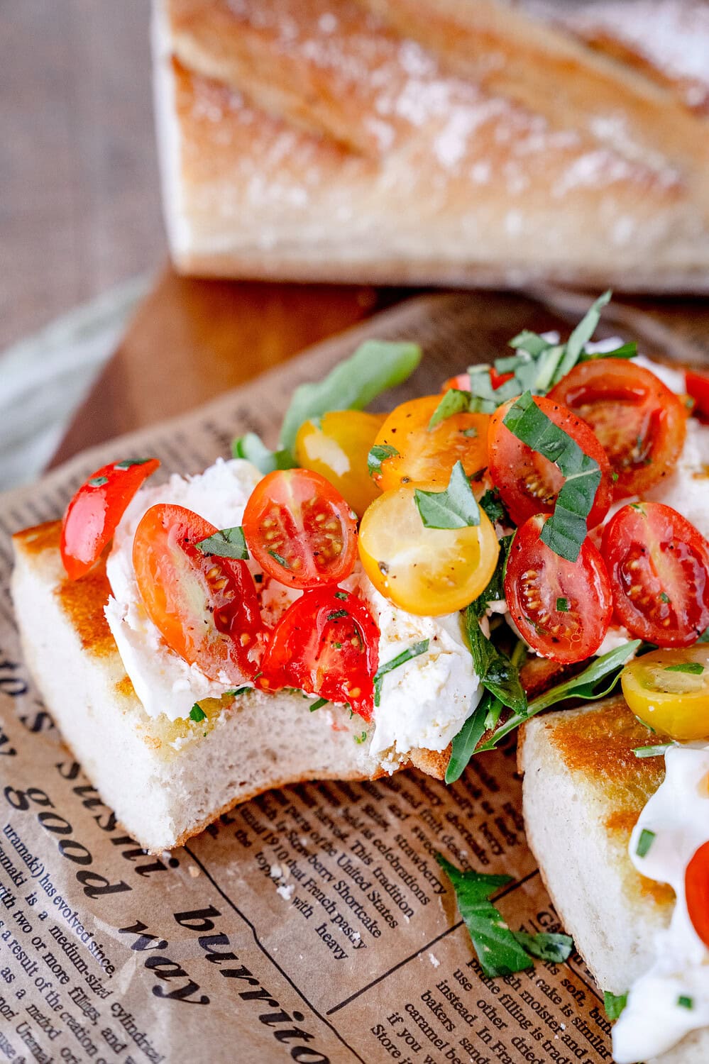 Angeröstetes Baguette mit Kirschtomaten und Burrata von dem schon eine Ecke abgebissen ist.