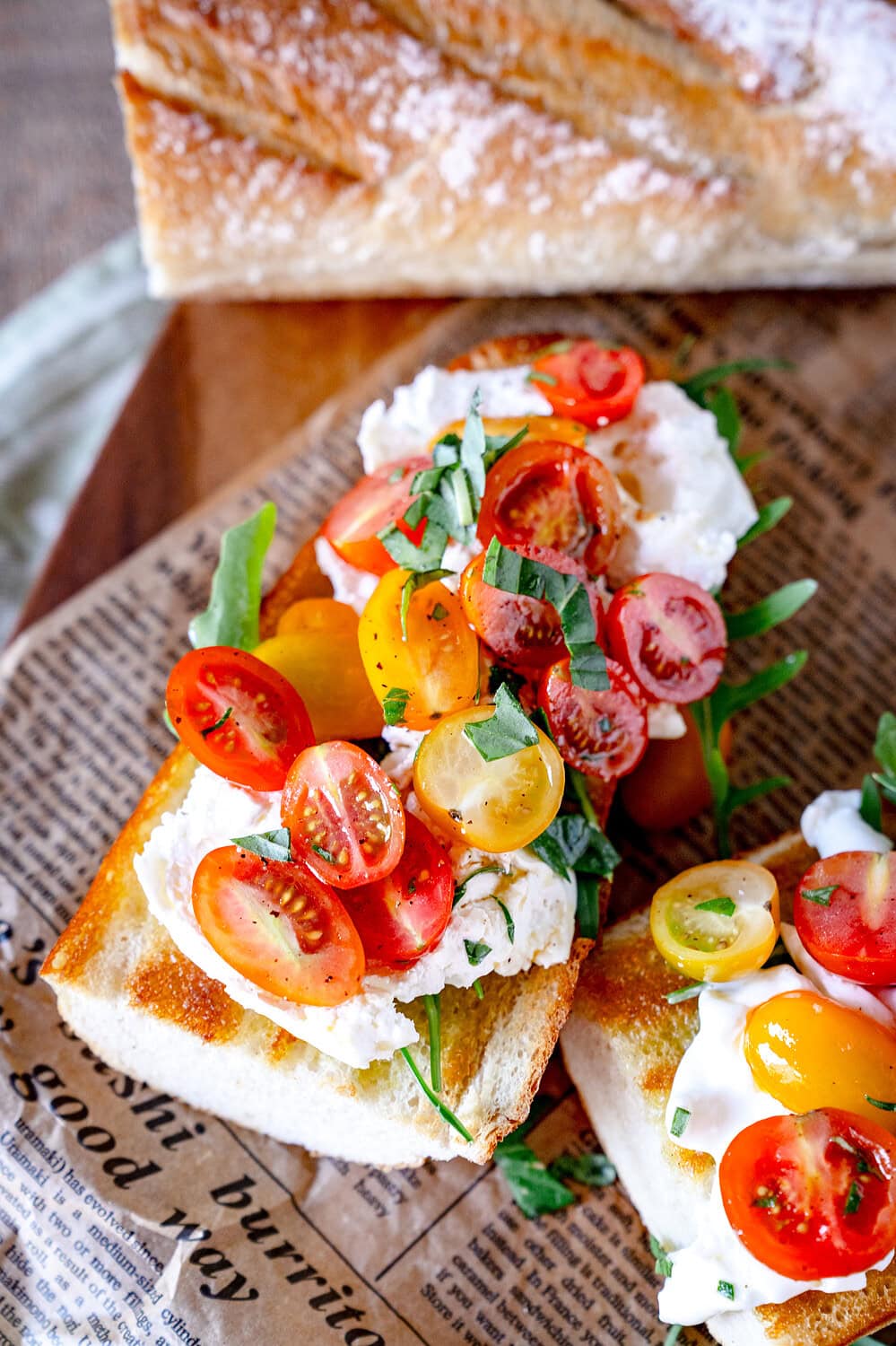 Burrata Baguette mit Kirschtomaten auf einem Holzbrett mit Weizenbaguette im Hintergrund