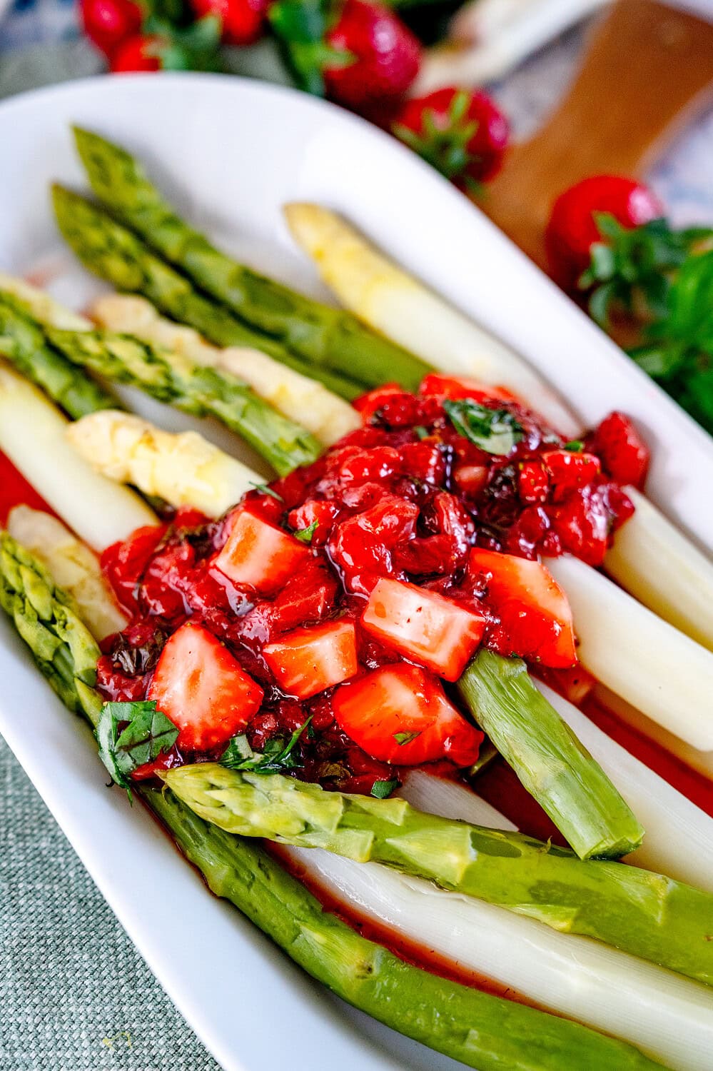 Nahaufnahme von einem länglichen Teller mit grünem und weißem Spargel. Darauf verteilt ist ein rotes Erdbeer Chutney
