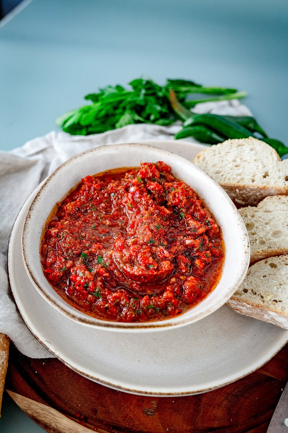 Acili Ezme in einer hellen Schale mit Baguette und Chillies im Hintergrund