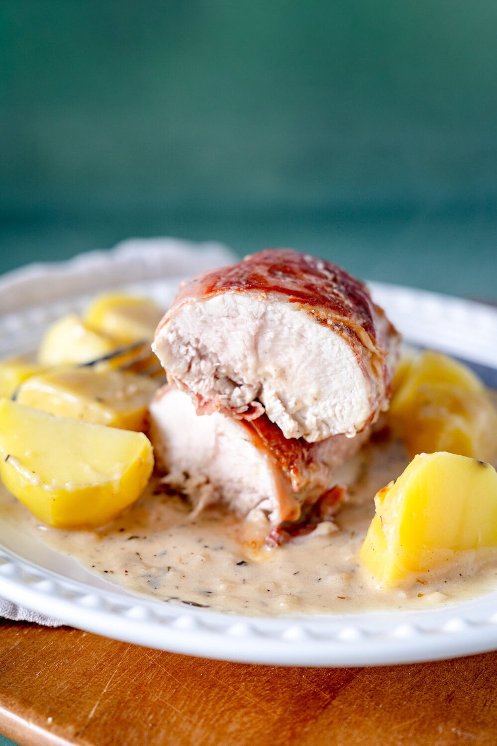 Aufgeschnittene Hähnchenbrust in Baconmantel auf Kartoffeln und mit einer Parmesansauce