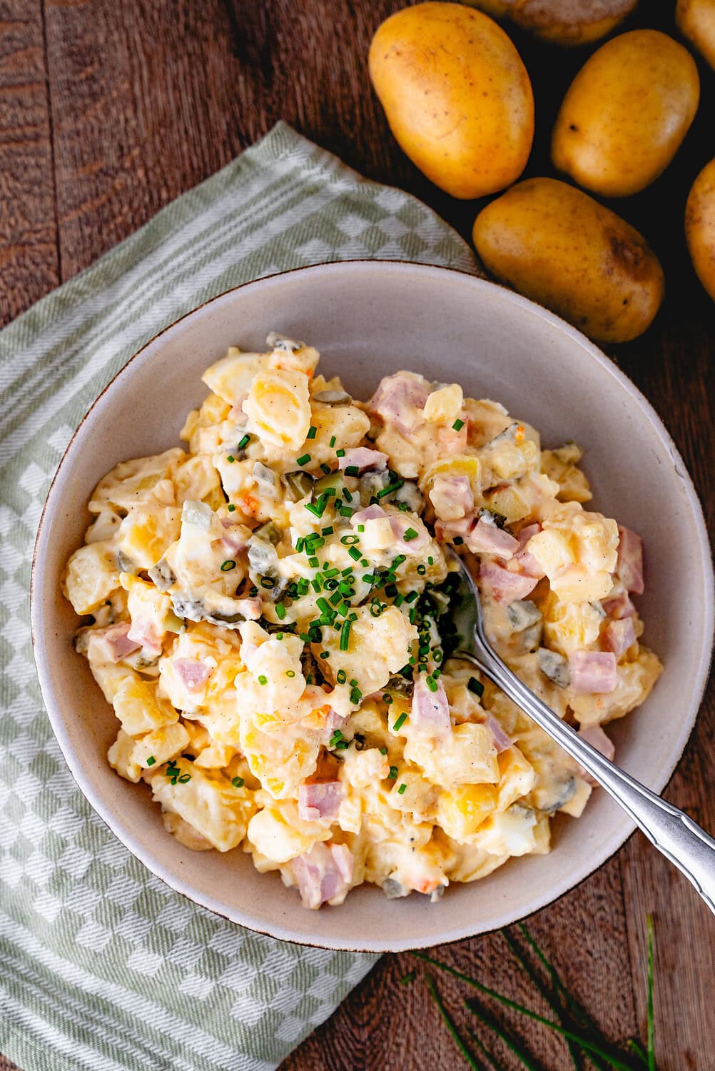 Kartoffelsalat mit Schinkenwurst und Schnittlauch auf einem Holzbrett mit grünem Tuch
