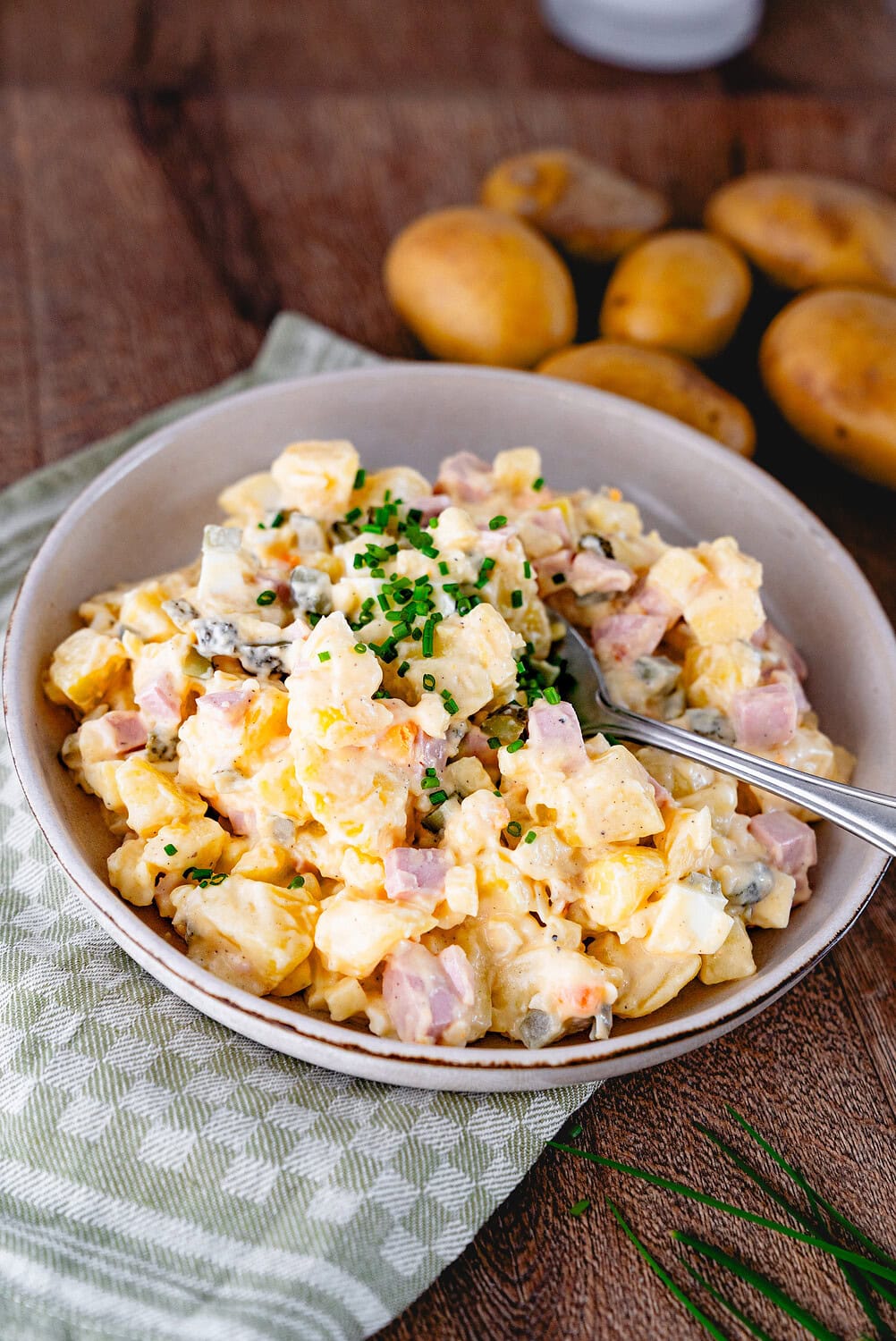 Oma Karolas Kartoffelsalat in einer Schüssel im Hintergrund sind Kartoffeln zu sehen
